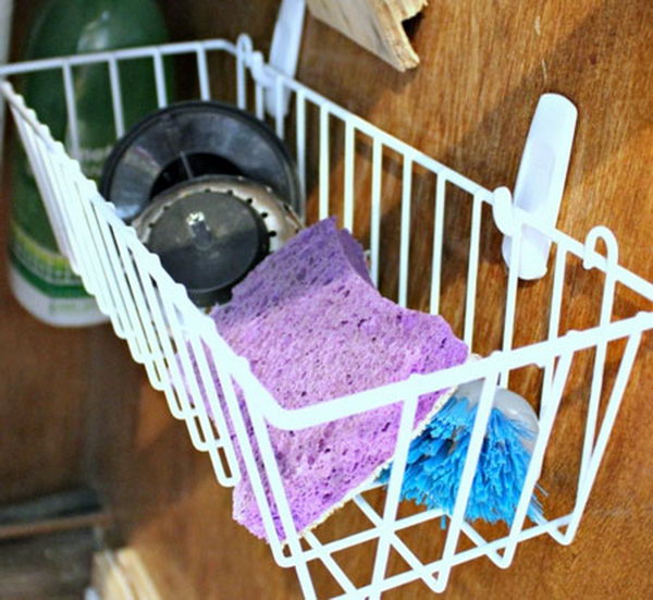 Hang a simple dollar store basket on the inside of your cabinet door. It's a clever under sink storage idea for wet sponges and brushes and give them air to dry.