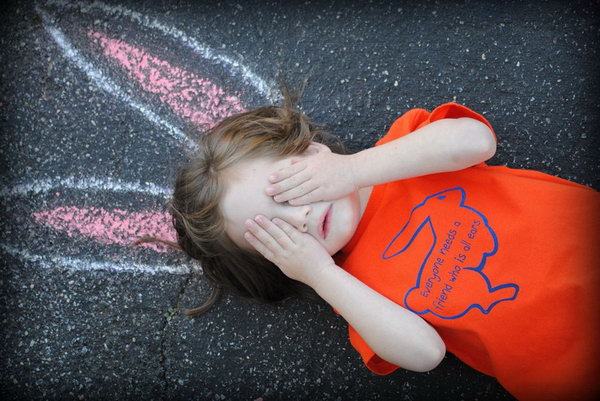 Funny Bunny Ears Easter Photo. The little girl wearing a red T shirt with a bunny patter is lying on the ground with the bunny ears drawing beforehand. I really love this Easter photo idea, it’s full of creation and imagination. 