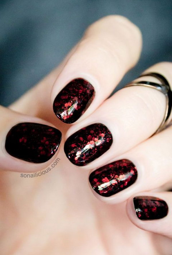 Uñas de base negra con brillo rojo oscuro.